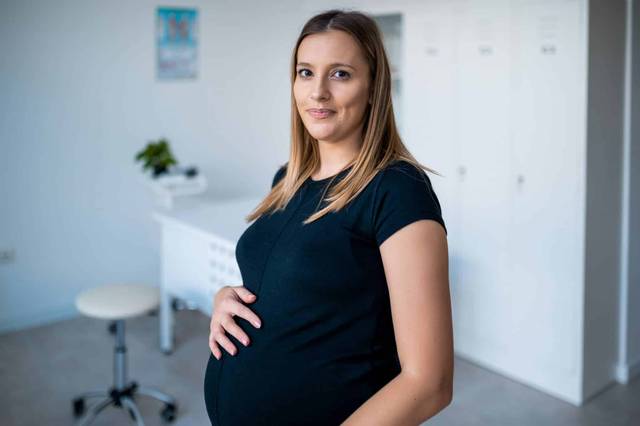 Femme enceinte debout, une main sur le ventre.