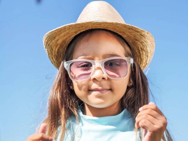 Portrait d'une jeune fille portant des lunettes de soleil et un chapeau en paille devant un ciel bleu clair