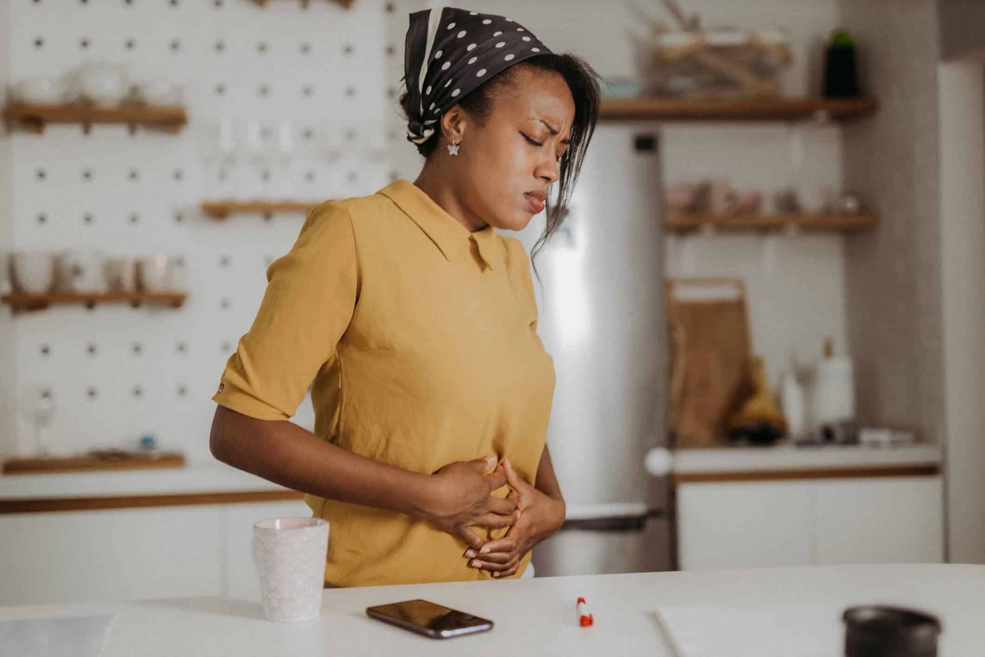 Femme debout dans une cuisine, les mains sur le ventre.