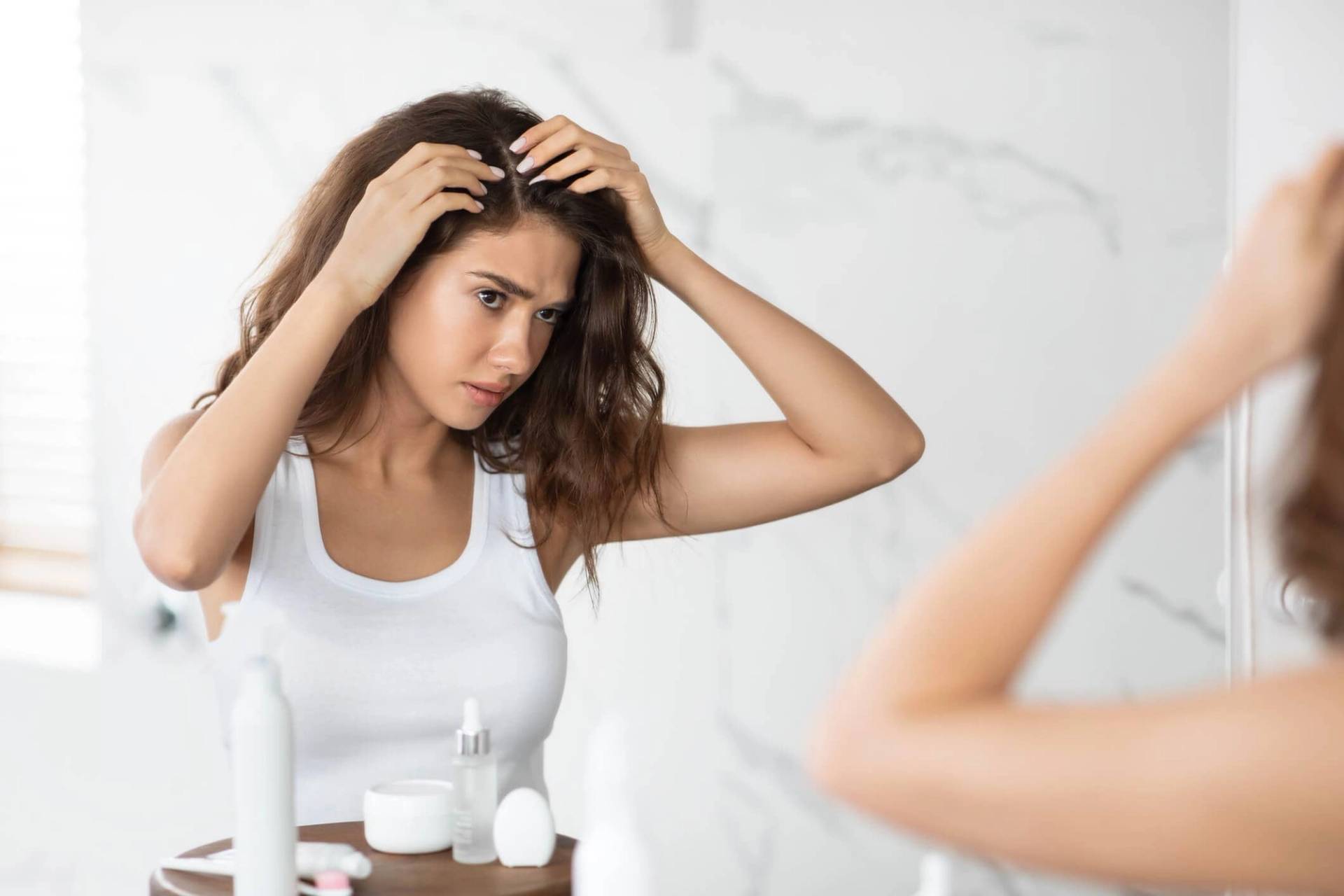 Femme examinant son cuir chevelu devant un miroir.