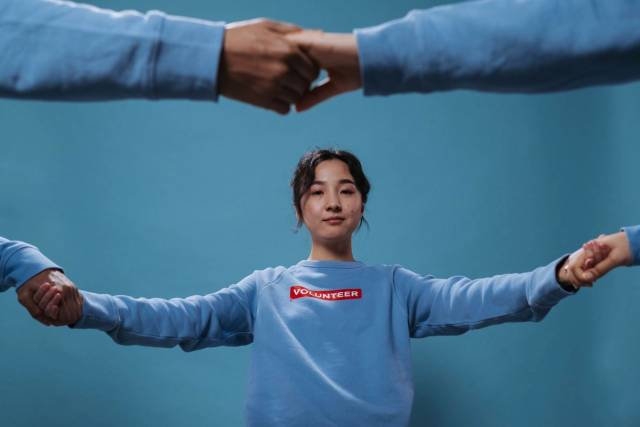 Femme asiatique en chemise de bénévolat bleue tenant des mains en cercle, symbolisant le travail d'équipe et la