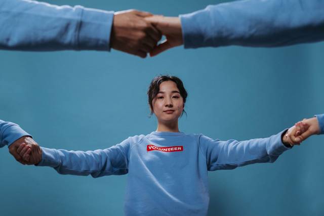 Femme asiatique en chemise de bénévolat bleue tenant des mains en cercle, symbolisant le travail d'équipe et la