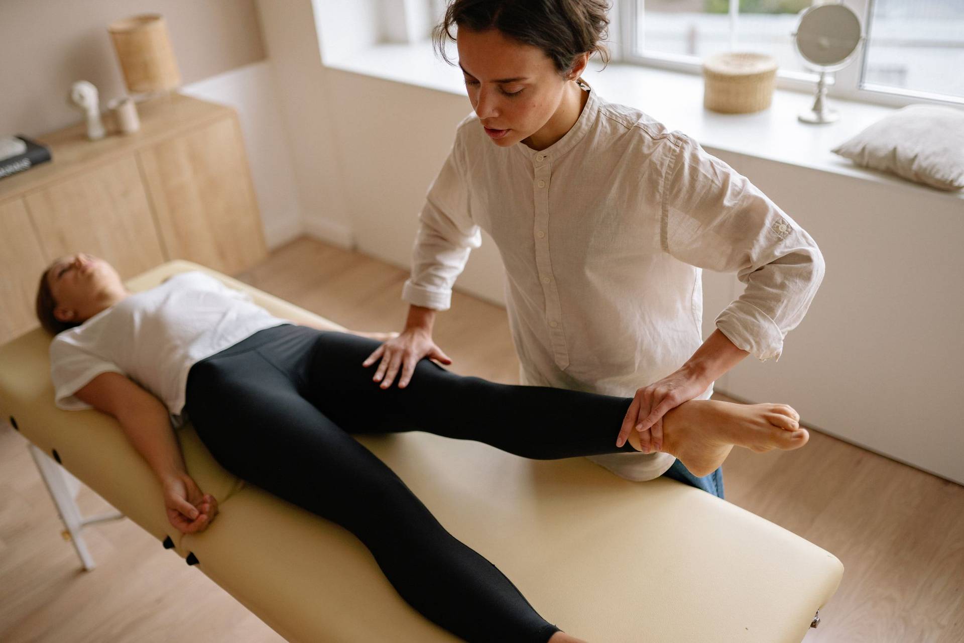Une kinésithérapeute accompagne une patiente pendant une séance de rééducation de la jambe.