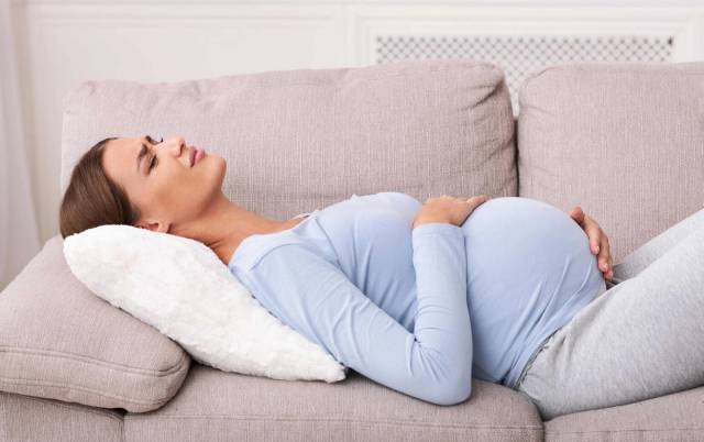 Femme allongée sur le dos sur un canapé avec un ventre enceinte