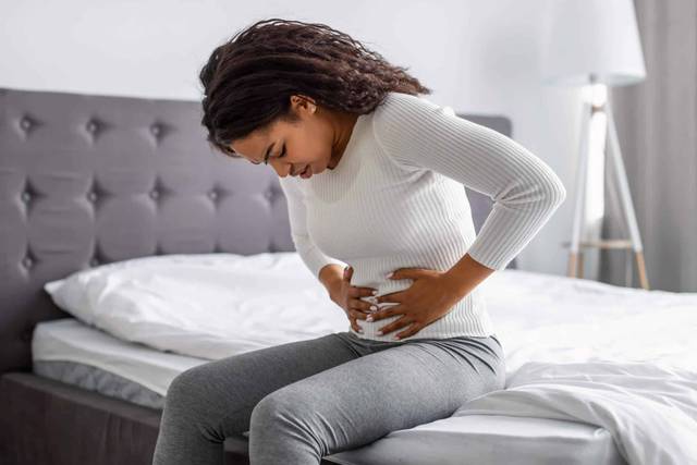 Femme assise au bord du lit, penchée sur son ventre.