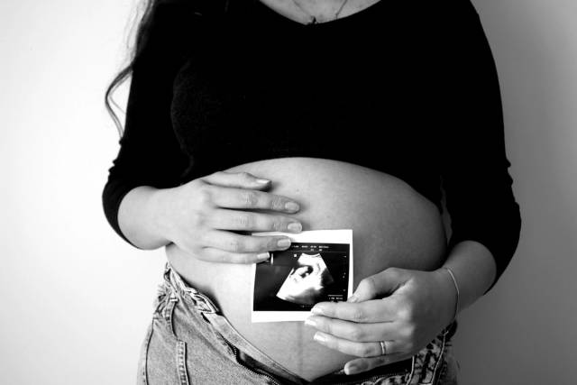 Une femme enceinte tient une photo d'échographie contre son ventre, symbolisant l'attente d'une maternité