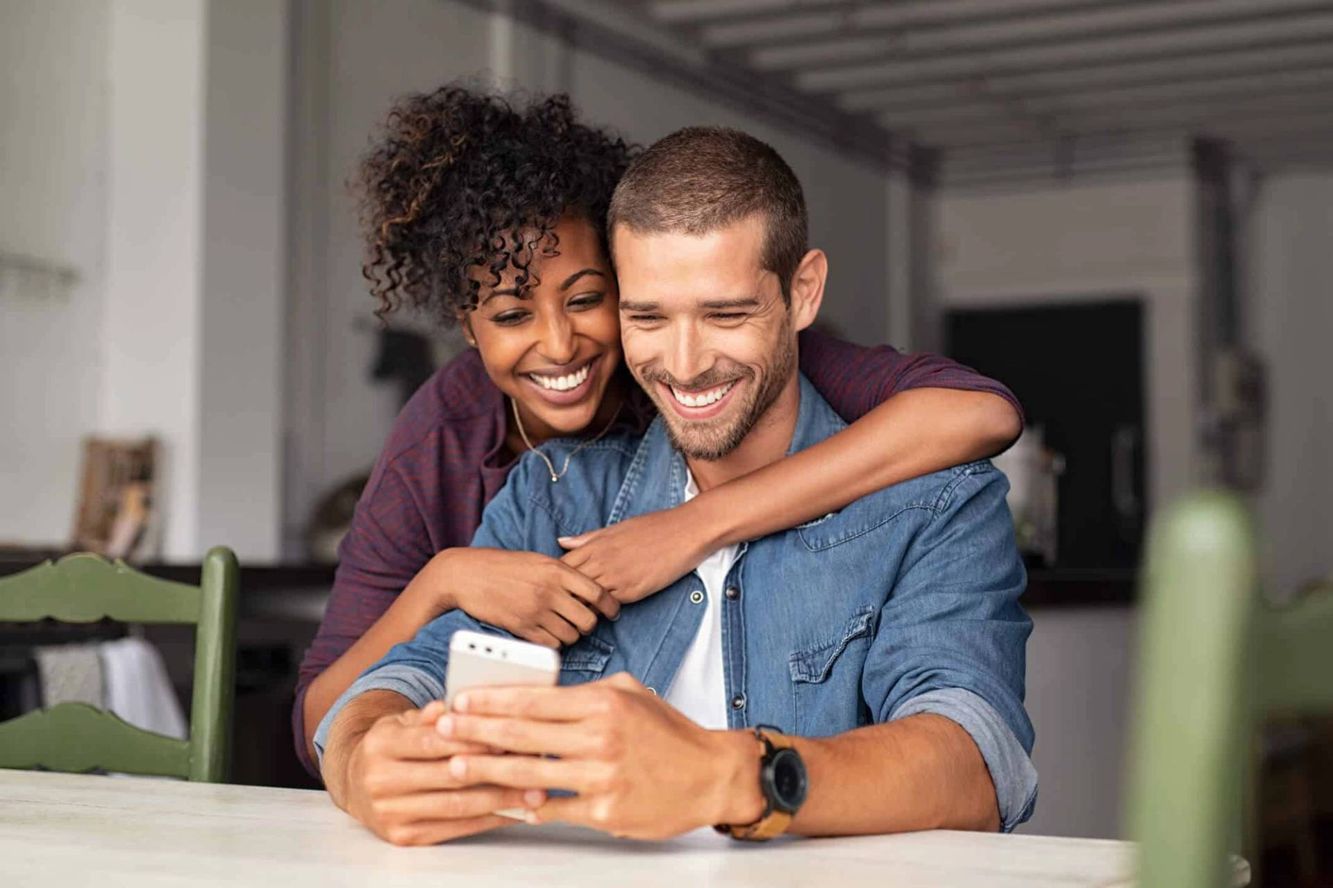 Deux personnes souriantes regardant ensemble un téléphone.