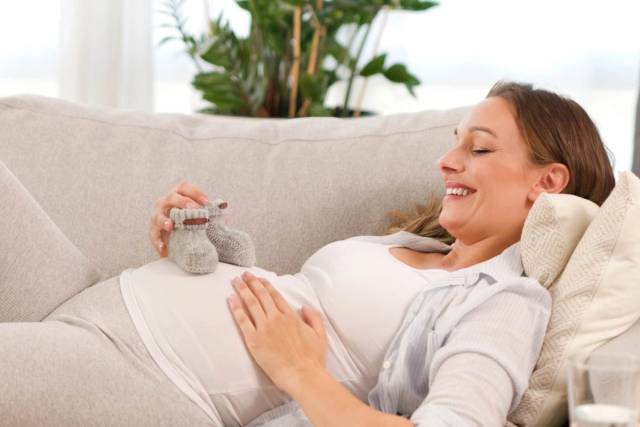 Femme au ventre arrondi allongée tenant de petits chaussons.