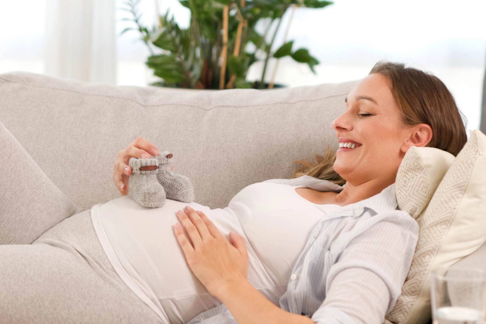 Femme au ventre arrondi allongée tenant de petits chaussons.