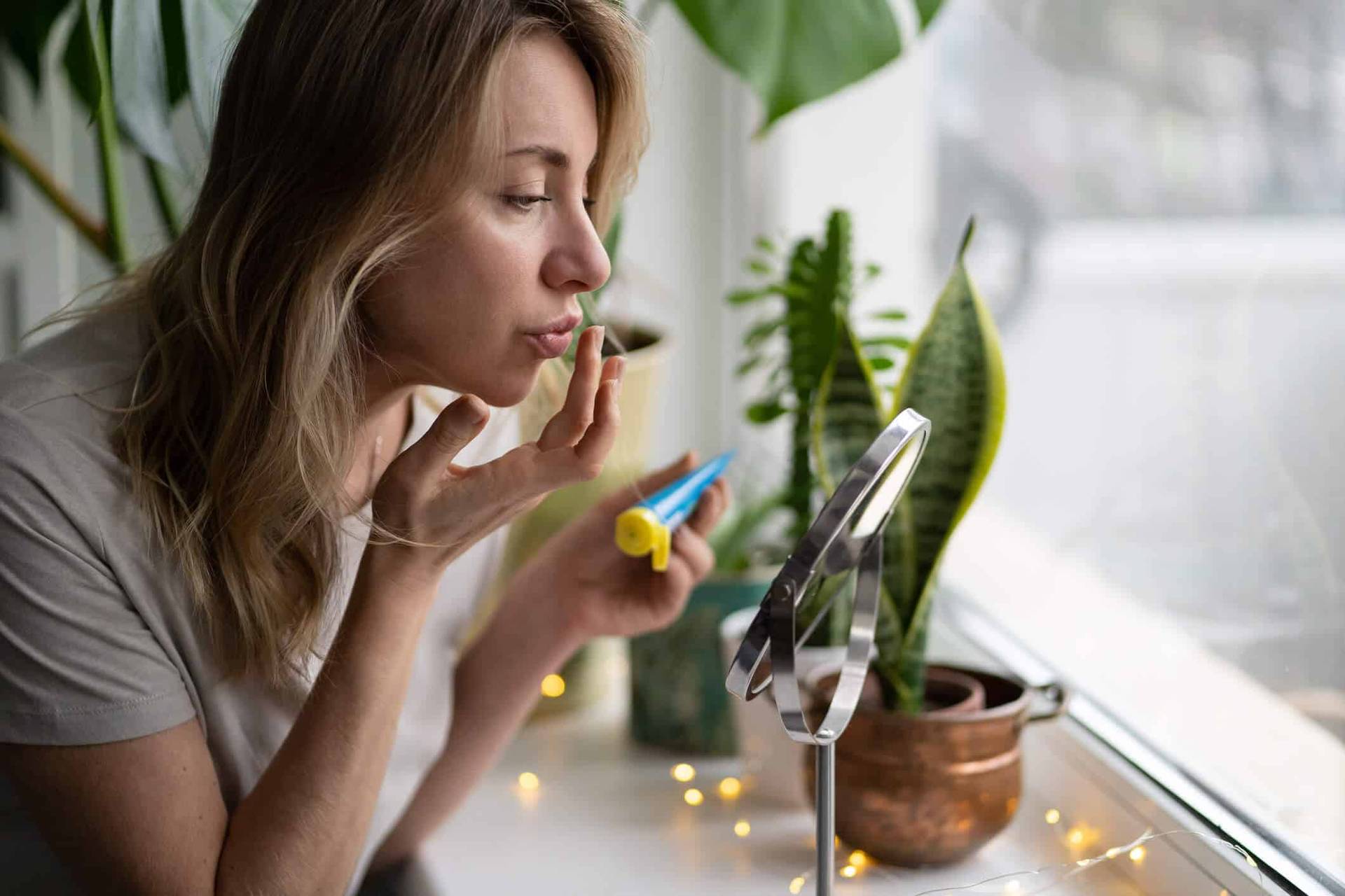 Femme appliquant un produit sur ses lèvres devant un miroir.