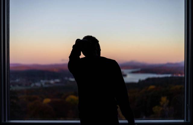 Une silhouette d'une personne à une fenêtre, contemplant un lac pittoresque et un paysage montagneux au coucher du