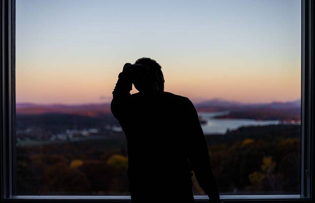Une silhouette d'une personne à une fenêtre, contemplant un lac pittoresque et un paysage montagneux au coucher du