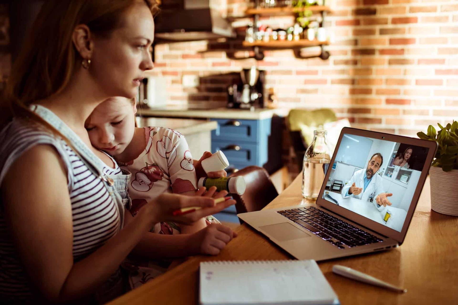 Adulte tenant un bébé pendant une consultation vidéo sur ordinateur.