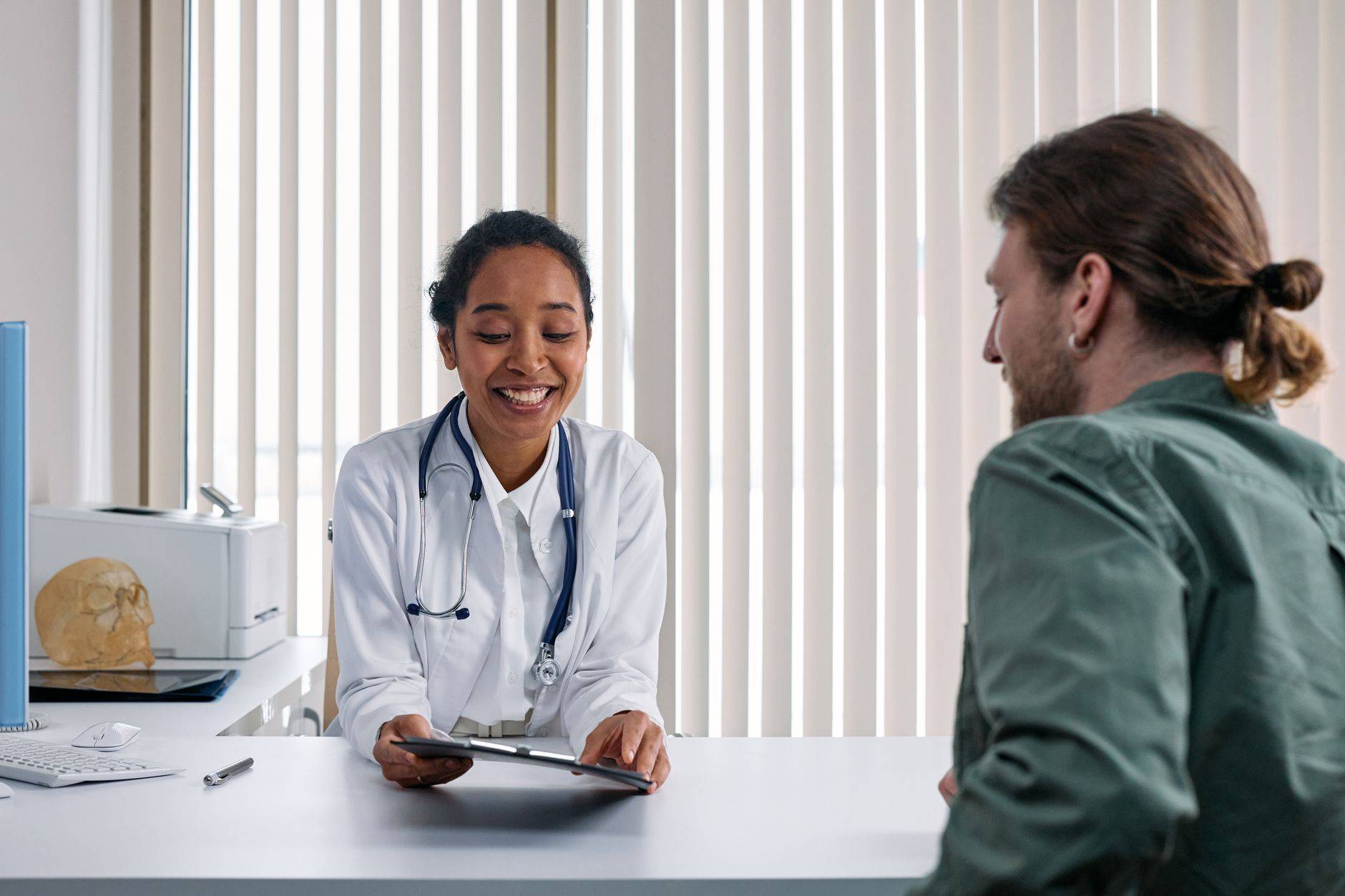Une médecin souriante échange avec un patient dans un cabinet lumineux.