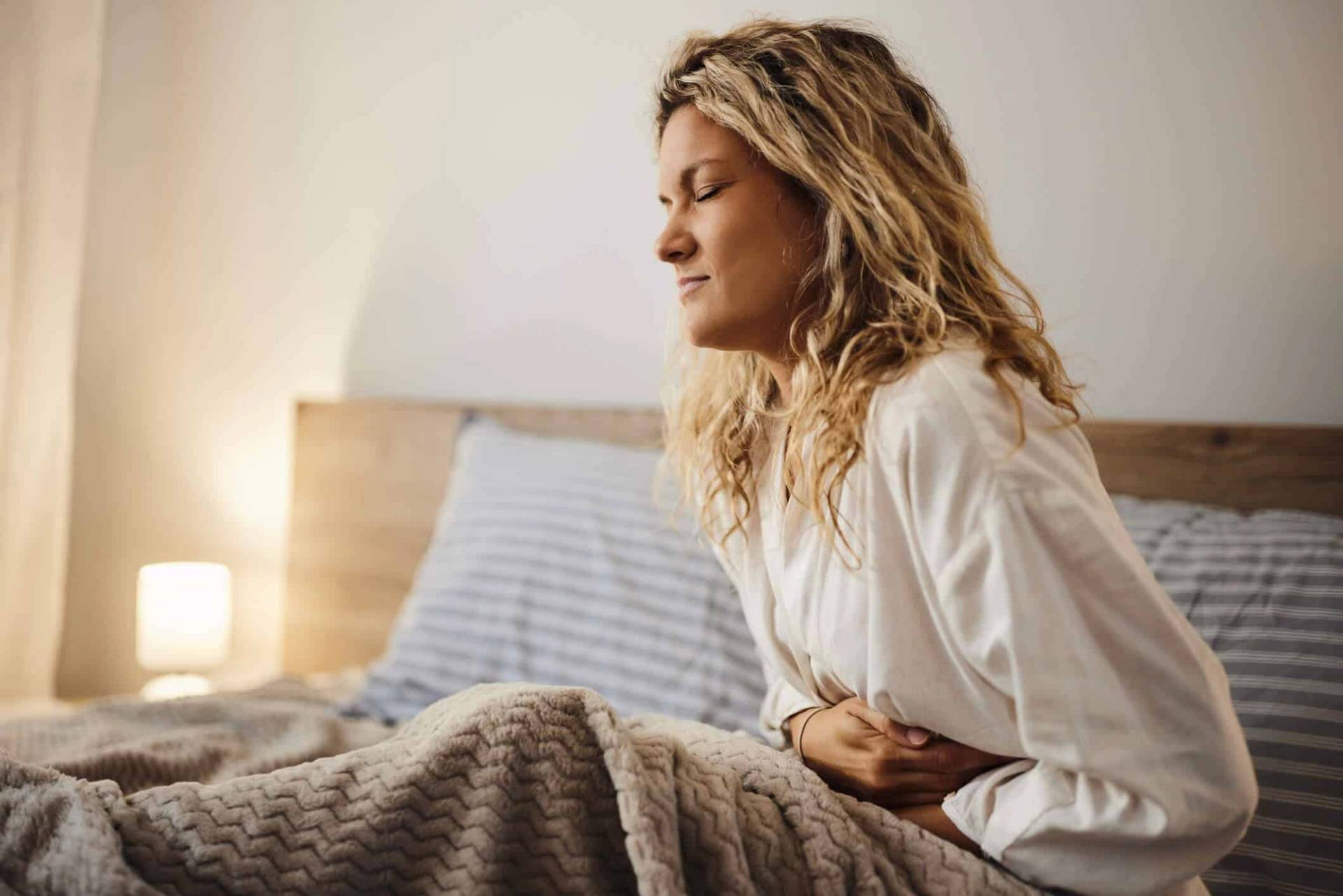 Femme assise dans un lit, une main sur le haut du ventre.