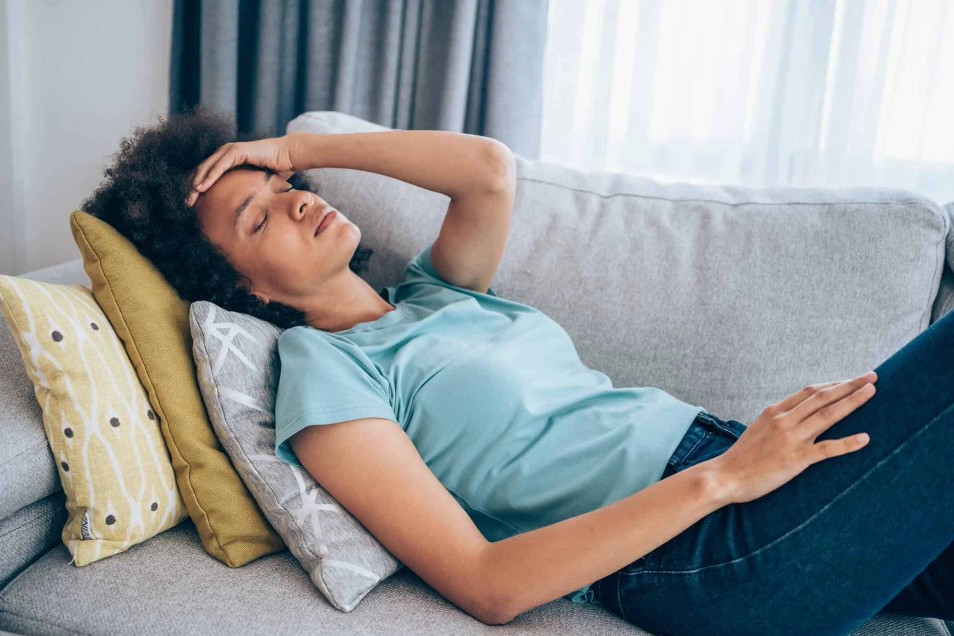 Femme allongée sur un canapé, une main sur le front.