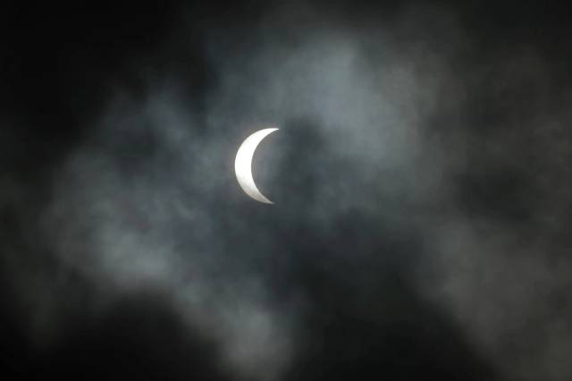 Éclipse partielle visible dans un ciel nuageux.