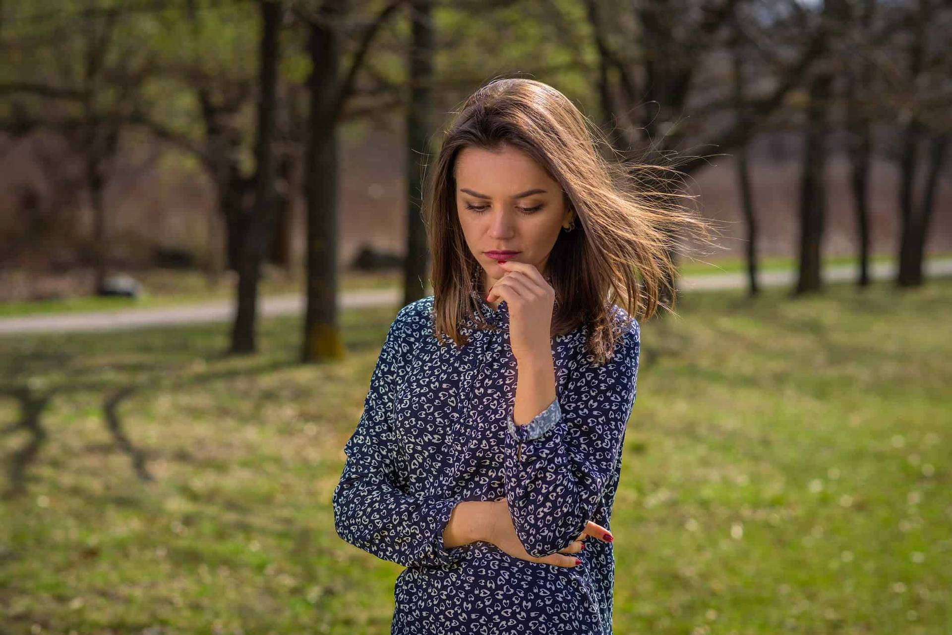 Femme debout dans un parc, une main sous le menton.