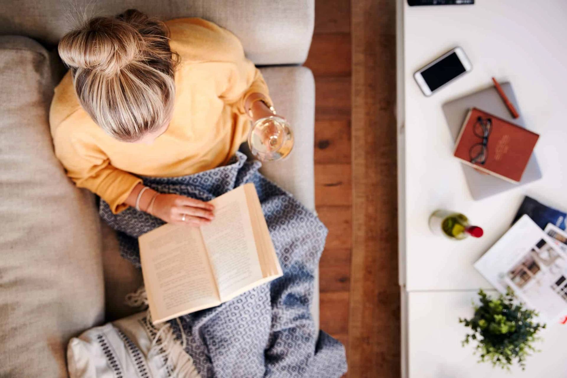 Personne lisant un livre sur un canapé, un verre à la main.