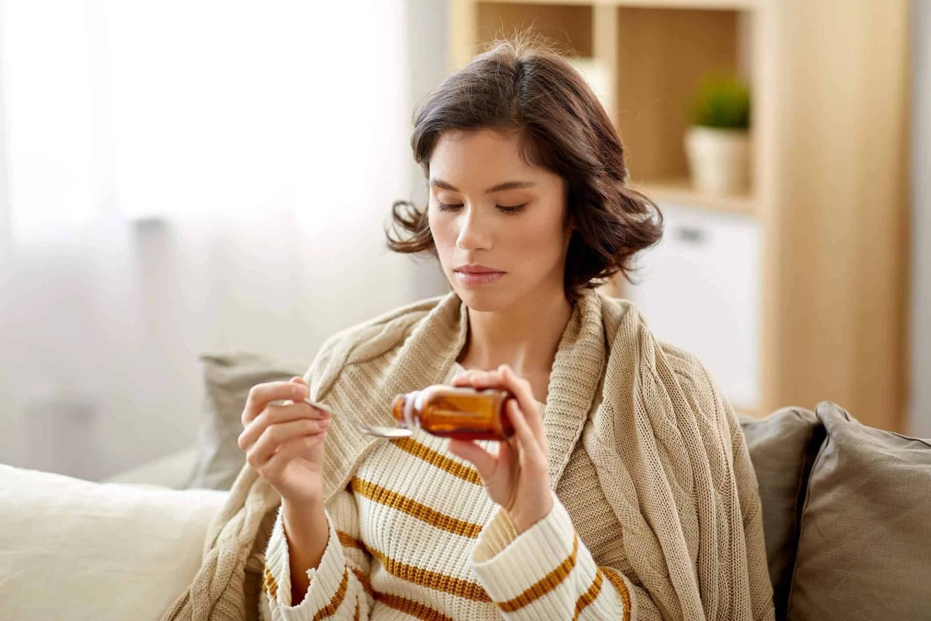 Femme emmitouflée tenant un pot de miel et une cuillère.