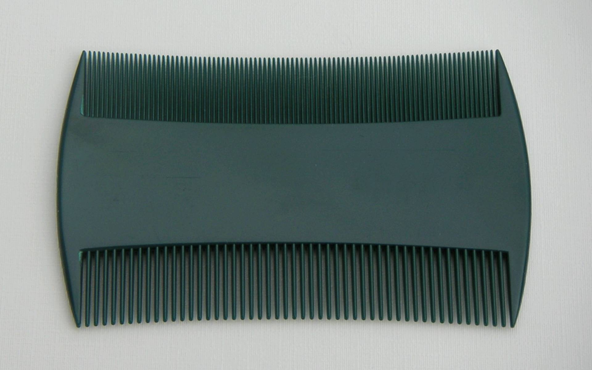 Peigne anti-poux à deux rangées de dents serrées, posé sur un fond clair.