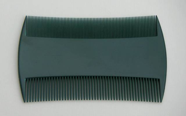 Peigne anti-poux à deux rangées de dents serrées, posé sur un fond clair.