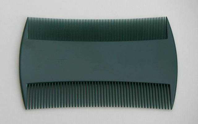Peigne anti-poux à deux rangées de dents serrées, posé sur un fond clair.