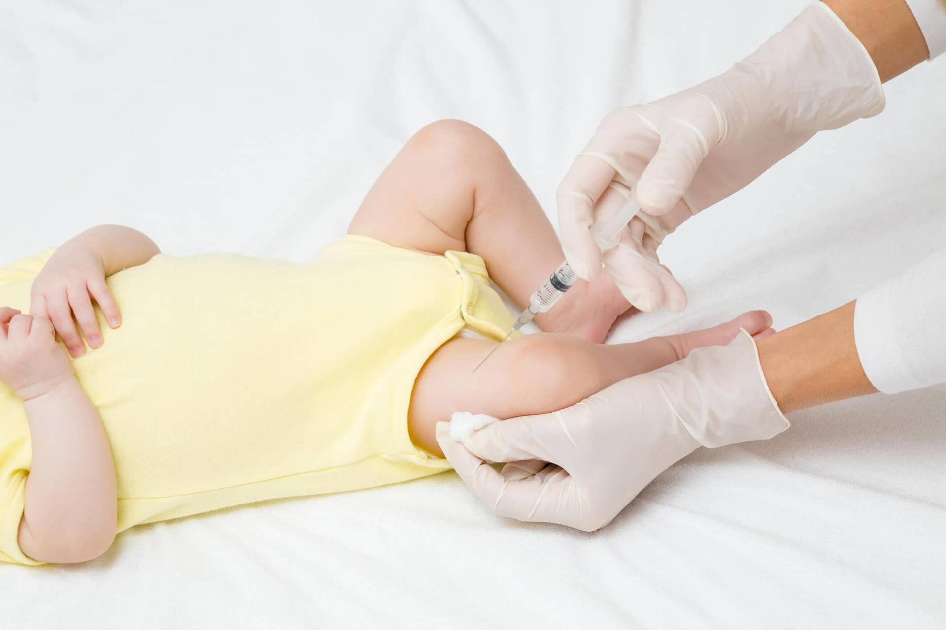 Mains gantées réalisant une injection dans la cuisse d’un nourrisson.