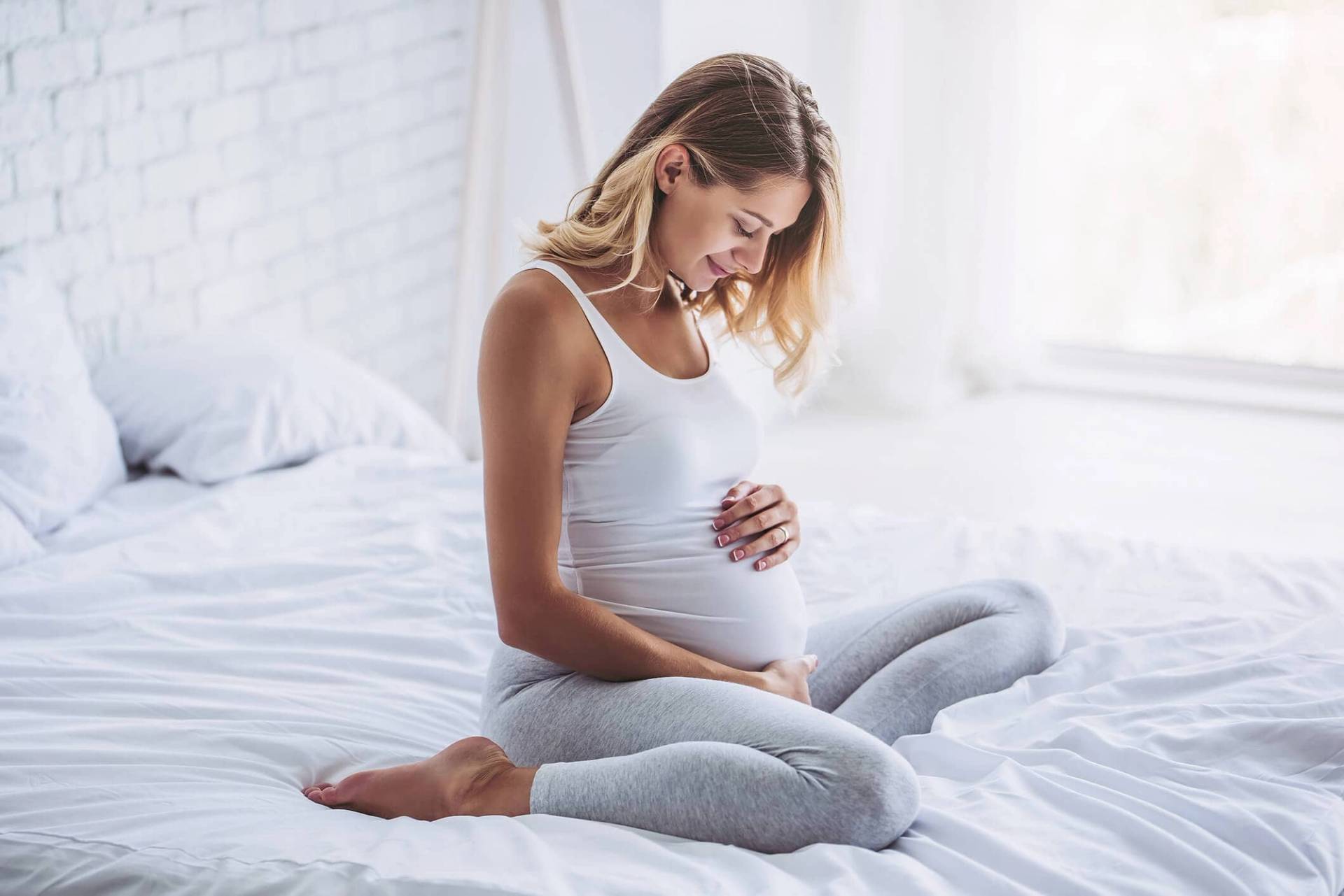 Femme au ventre arrondi assise sur un lit.