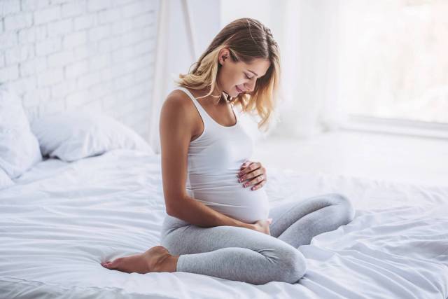 Femme au ventre arrondi assise sur un lit.