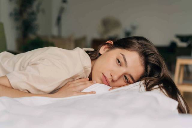 Femme allongée sur un lit, les yeux ouverts.