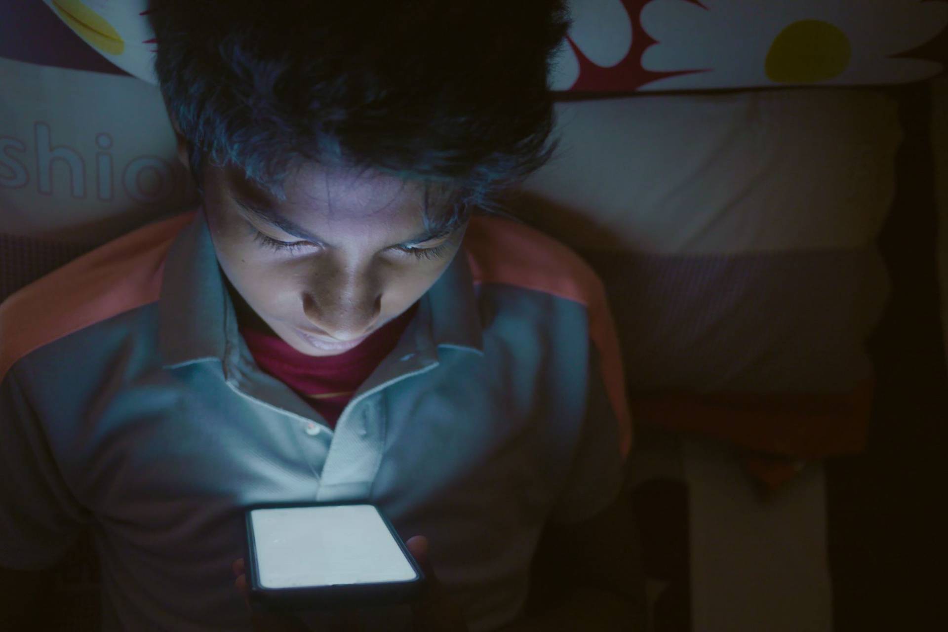 Garçon allongé sur le lit, regardant intensément un écran de smartphone lumineux