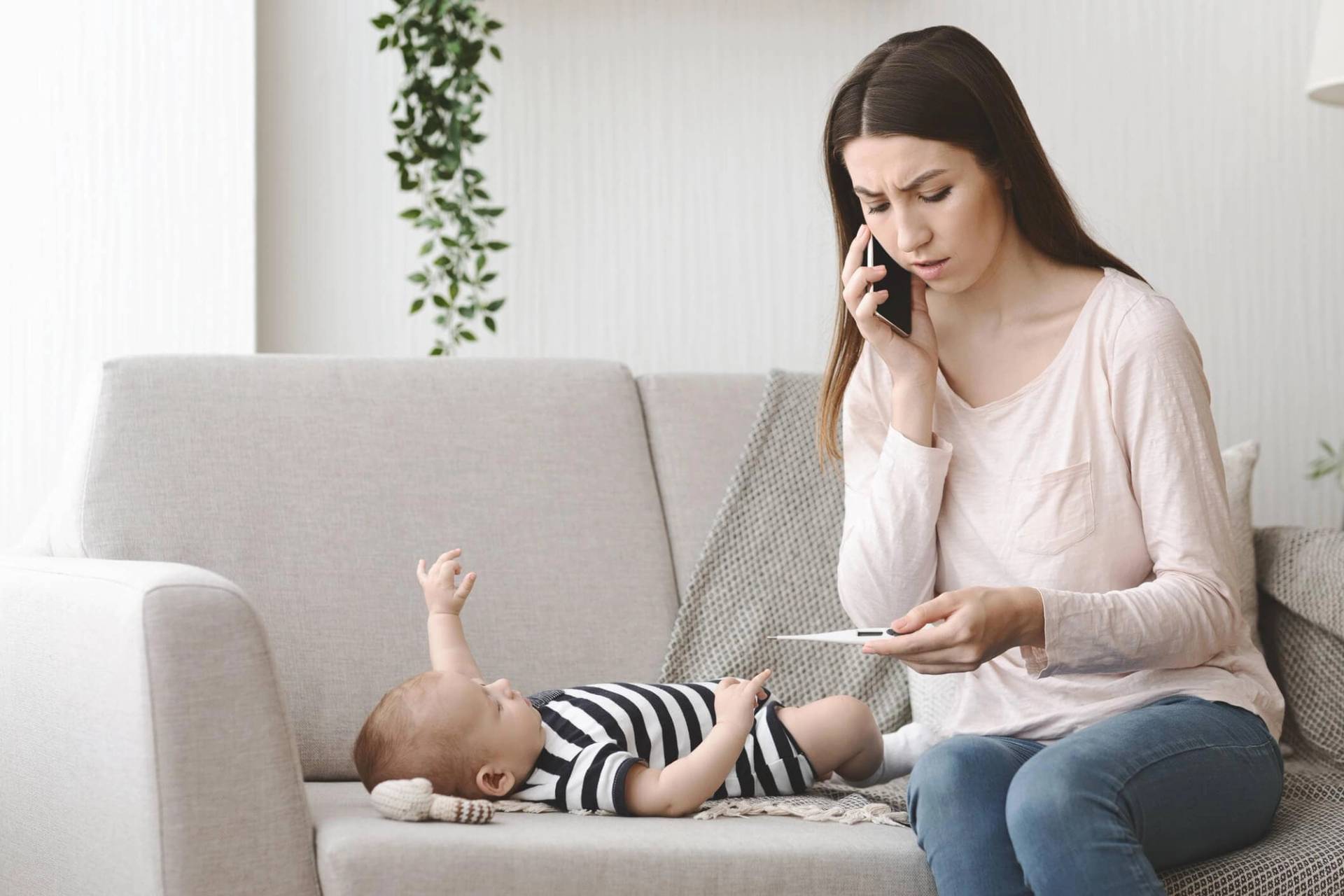Adulte tenant un thermomètre et téléphonant près d’un bébé.
