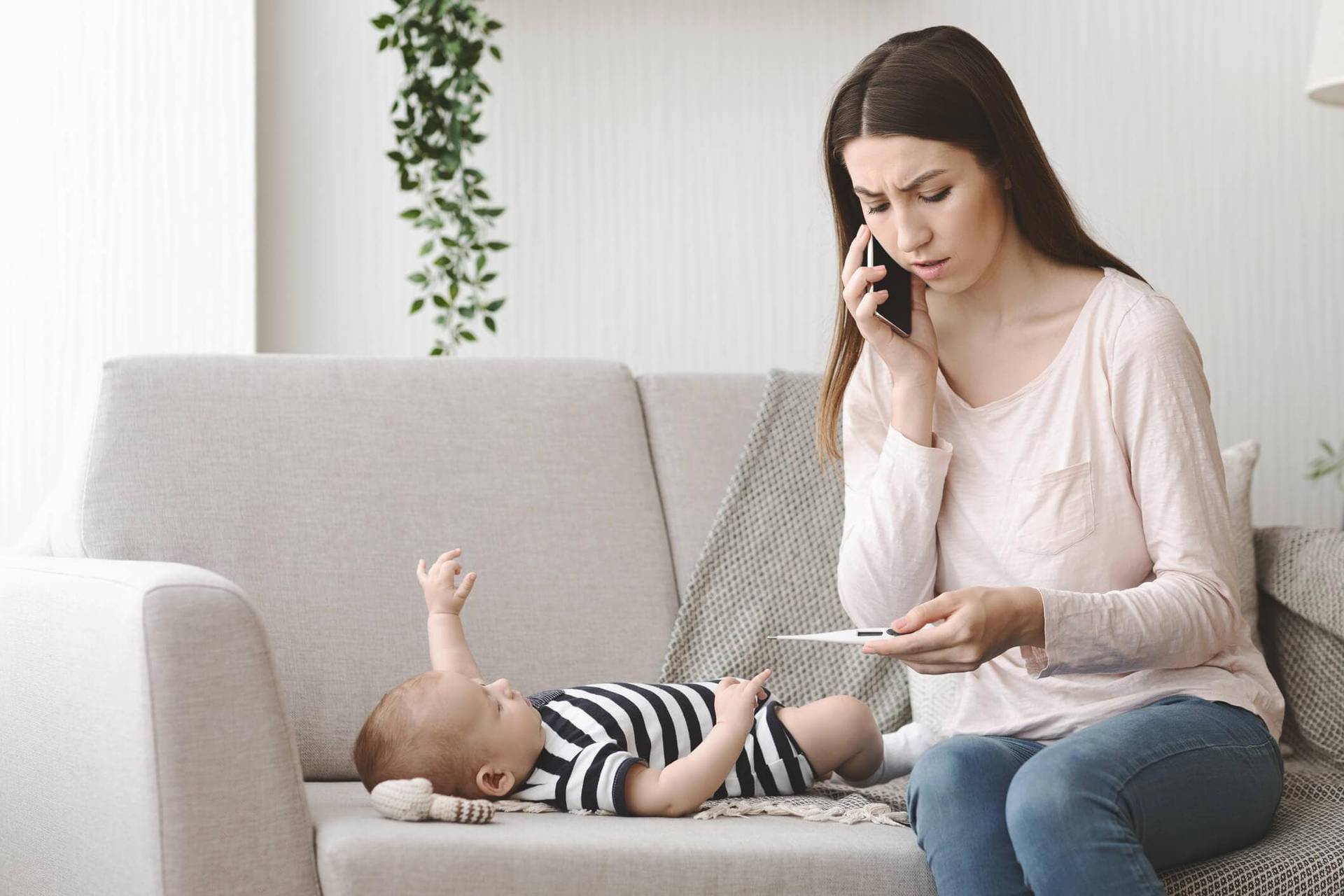 Adulte tenant un thermomètre et téléphonant près d’un bébé.