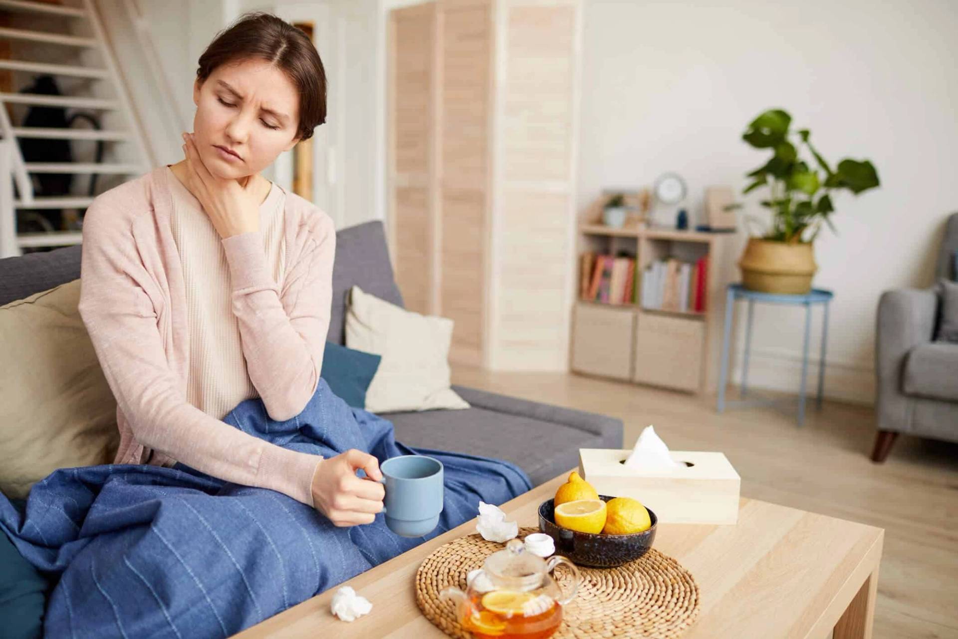 Femme assise sous une couverture, une main à la gorge, avec une tasse.