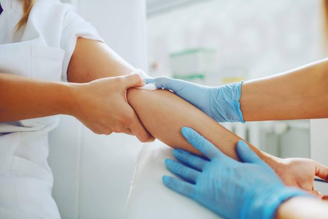 Mains gantées manipulant le bras d’une personne pendant un prélèvement.