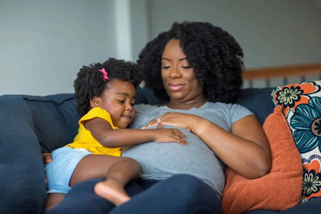 Femme au ventre arrondi assise avec un enfant.