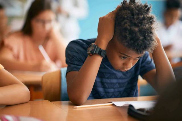 Enfant à son bureau dans une classe, les mains sur la tête.