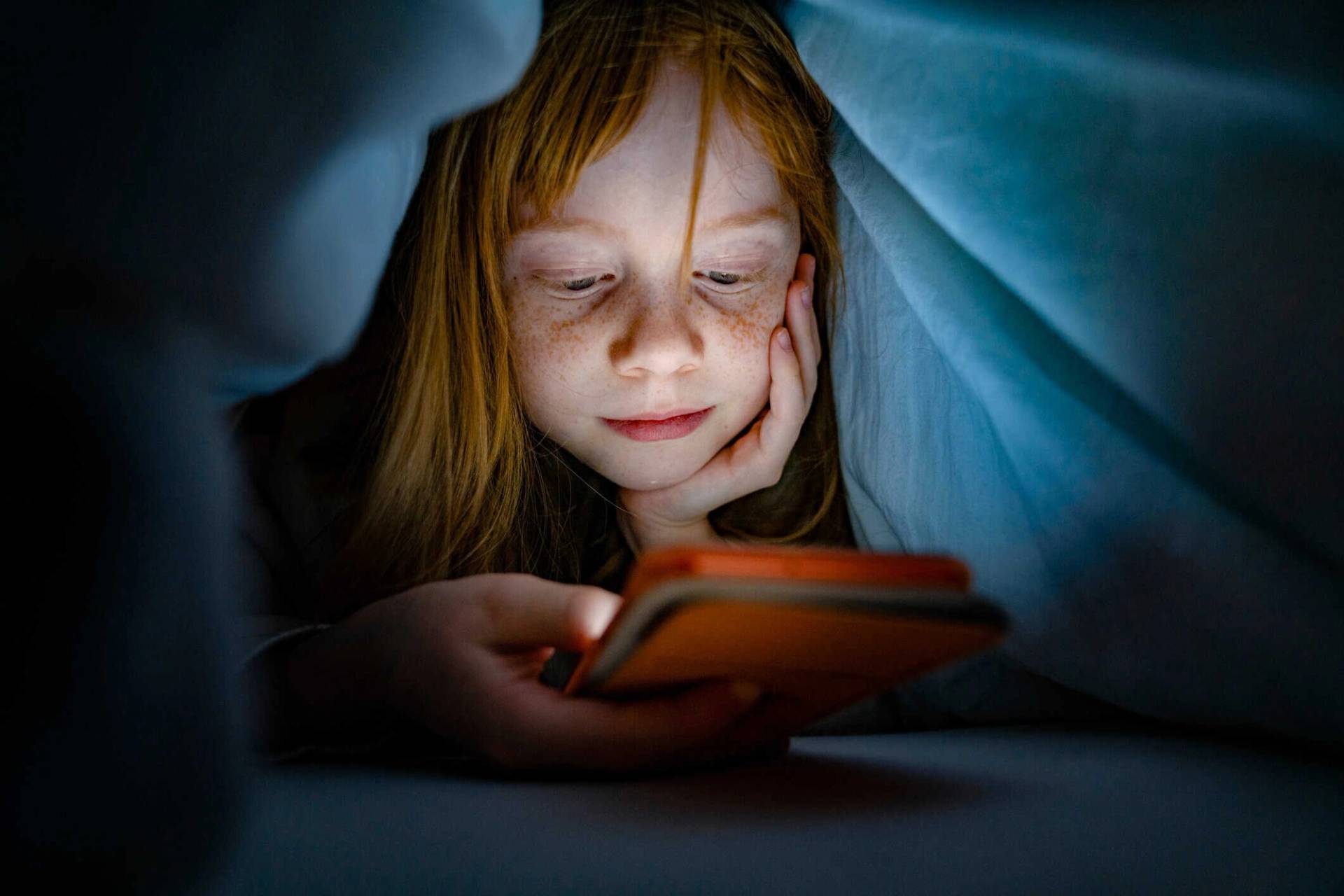 Enfant sous une couverture regardant un écran.