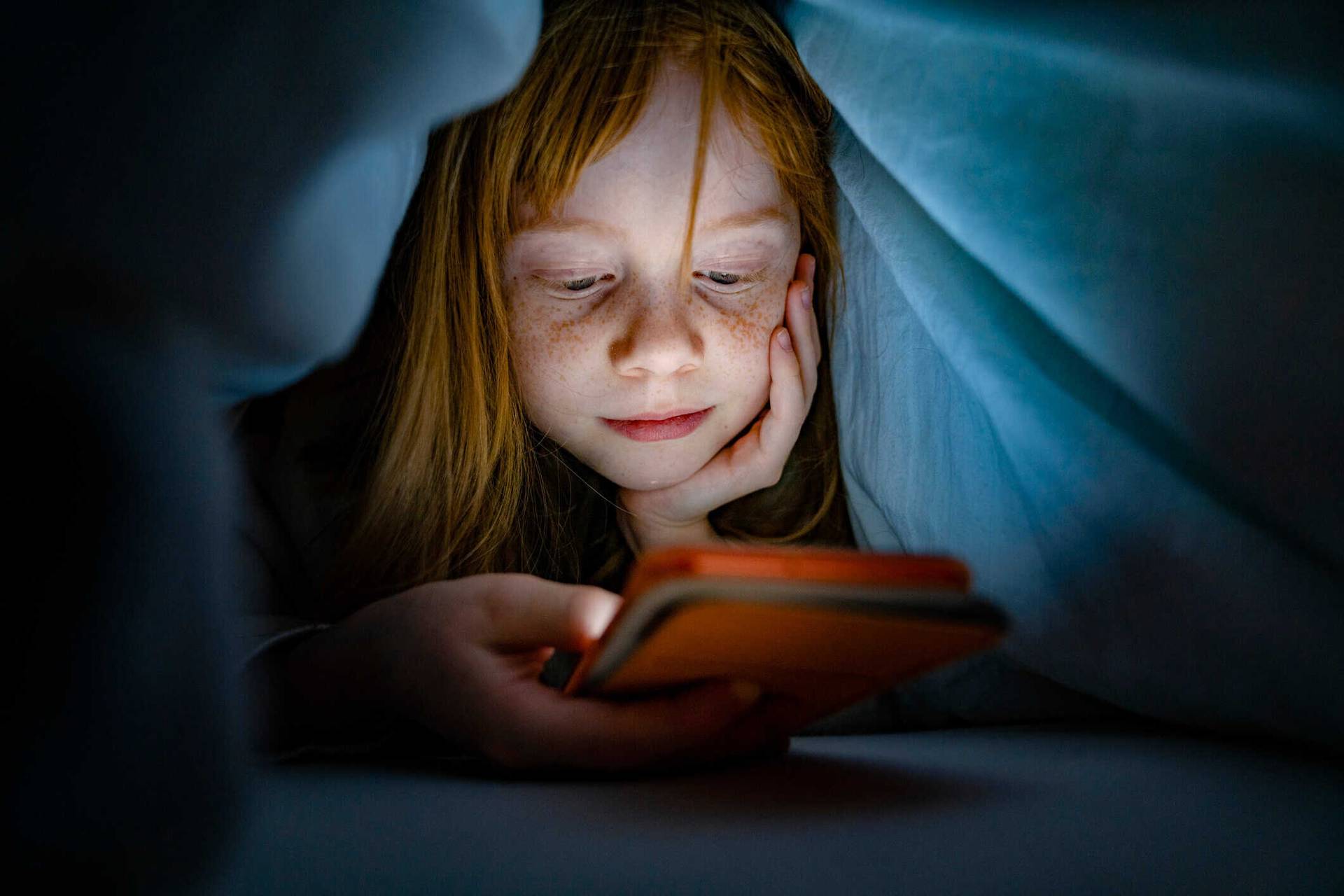 Enfant sous une couverture regardant un écran.