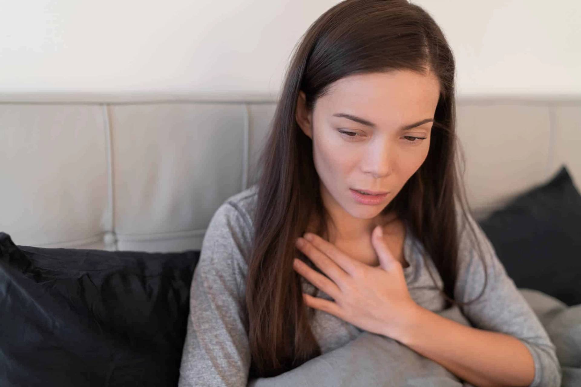 Femme assise sur un lit, une main sur la poitrine.