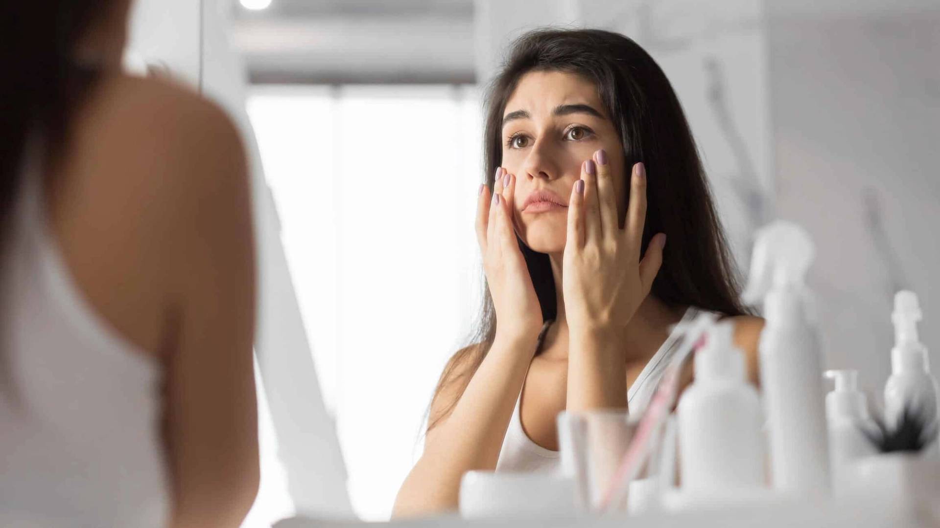 Femme appliquant un produit sur son visage devant un miroir.