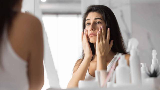 Femme appliquant un produit sur son visage devant un miroir.