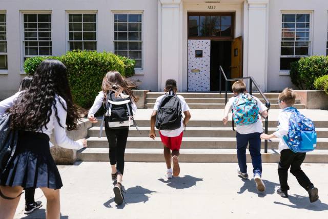 Groupe d'étudiants avec des sacs à dos courant vers l'école, capturé de derrière, montrant de l'excitation