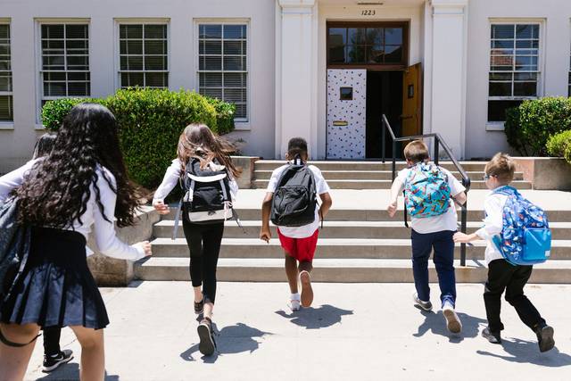 Groupe d'étudiants avec des sacs à dos courant vers l'école, capturé de derrière, montrant de l'excitation