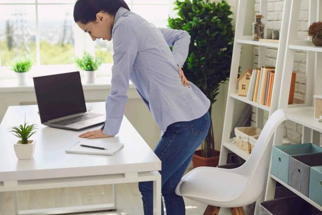 Personne se levant d’une chaise de bureau, une main sur le bas du dos.