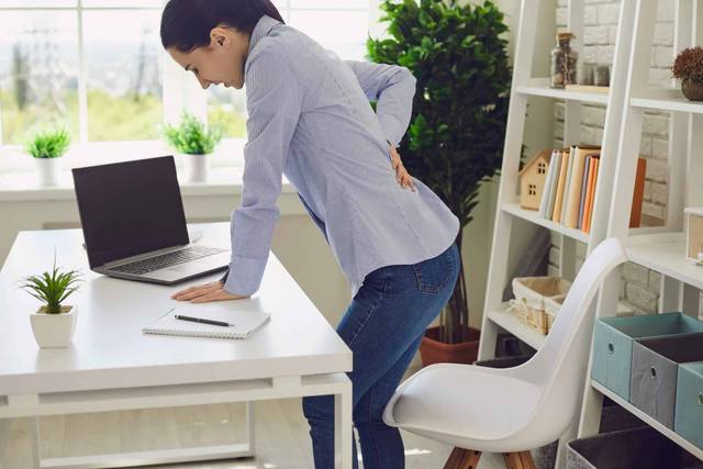 Personne se levant d’une chaise de bureau, une main sur le bas du dos.
