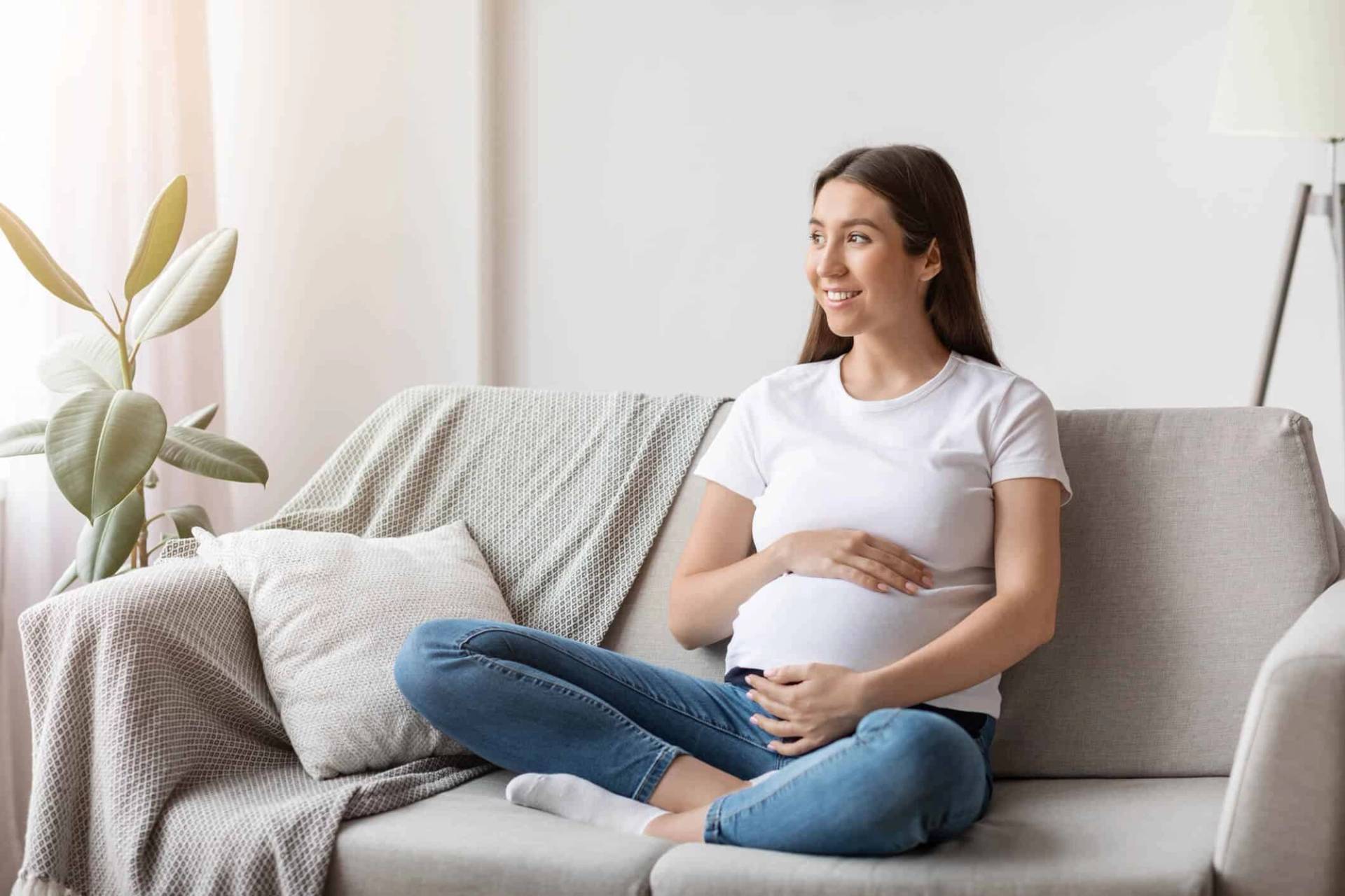 Femme au ventre arrondi assise en tailleur sur un canapé.