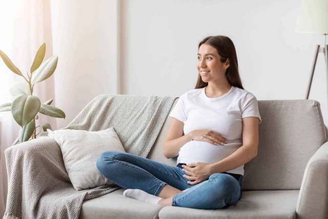 Femme au ventre arrondi assise en tailleur sur un canapé.