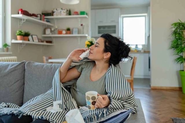 Femme utilisant un spray nasal sur un canapé.